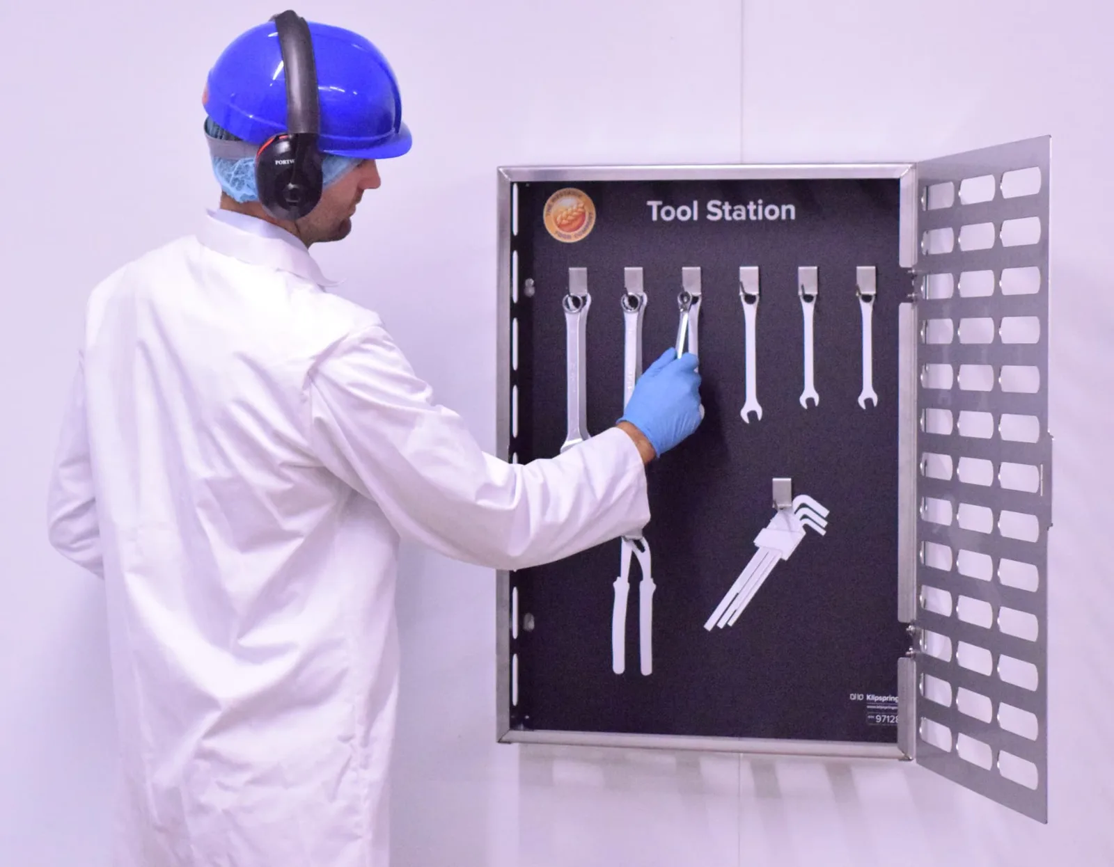 Operator in PPE taking a spanner from an open stainless steel tool cabinet with shadowed positions