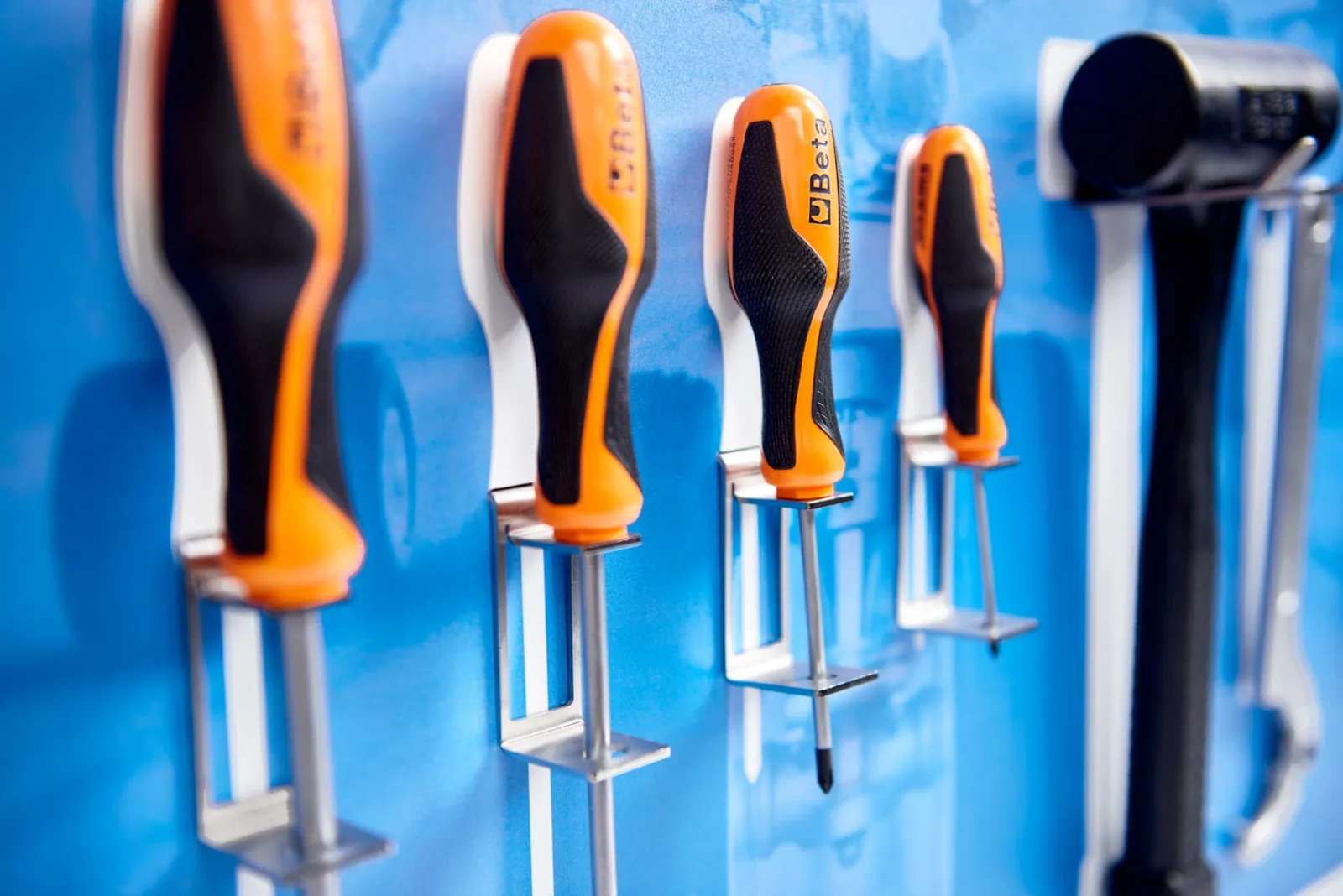 Close-up of screwdrivers and a hammer held in stainless clips on a blue board