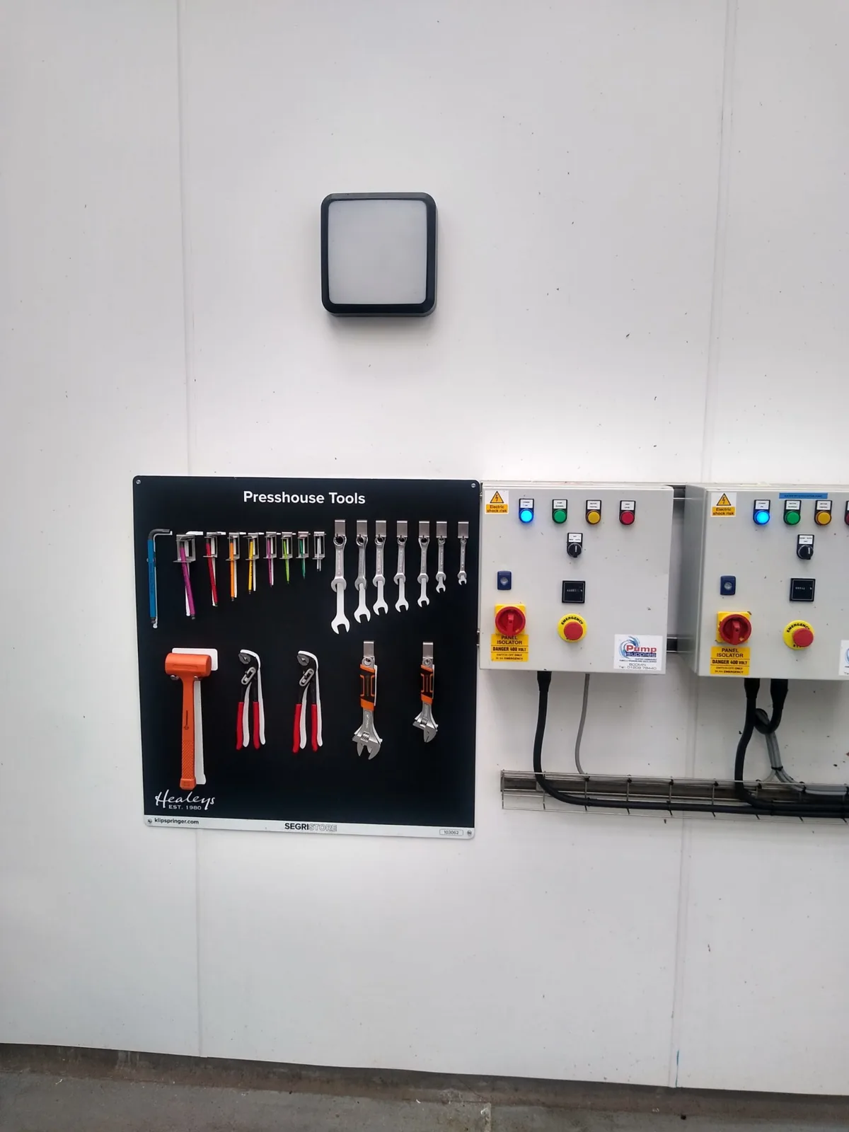 Wall-mounted presshouse tool shadow board holding spanners, hex keys, pliers and a mallet next to pump control panels